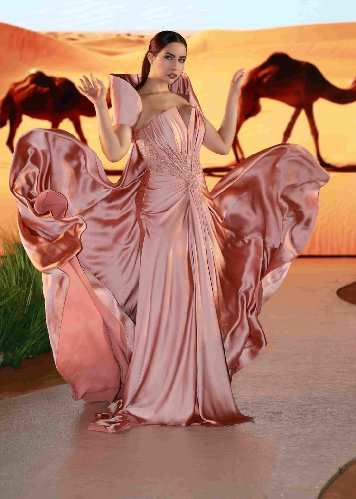 Woman in flowing pink gown posing in desert sunset.