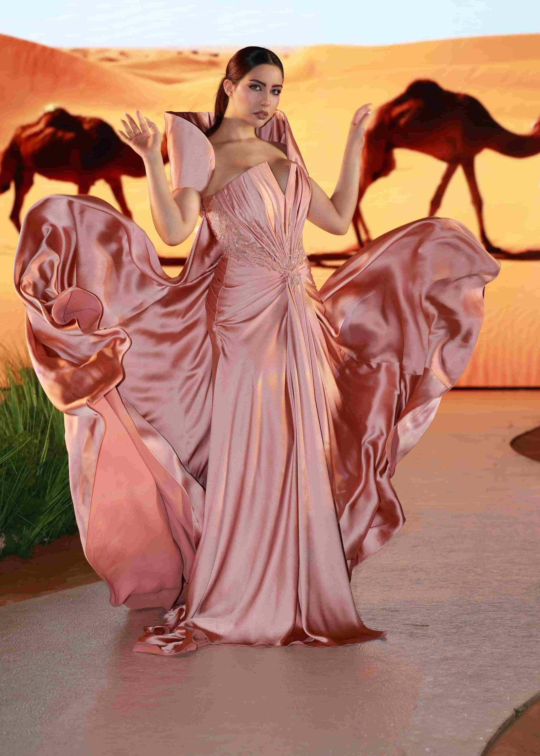 Woman in flowing pink gown posing in desert sunset.