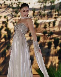 Elegant woman wearing a shimmering silver gown posing gracefully against a desert backdrop in Dubai.