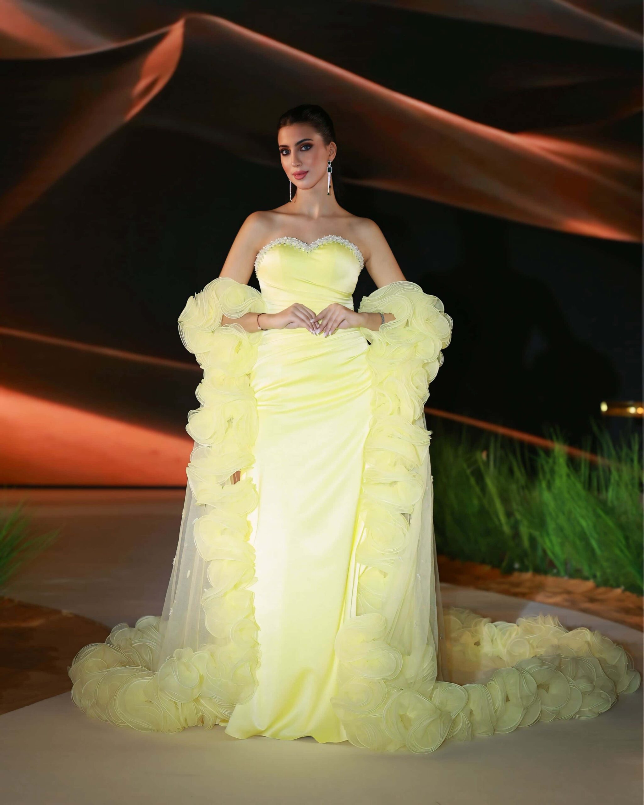 Elegant woman in a yellow evening gown posing confidently on a runway.