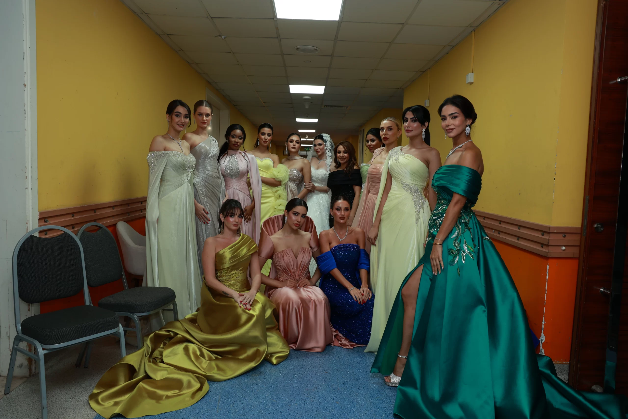 Group of fashion models wearing elegant hand-embroidered evening gowns in pastel and jewel tones, showcasing Sophia Bognem couture designs backstage in Abu Dhabi.